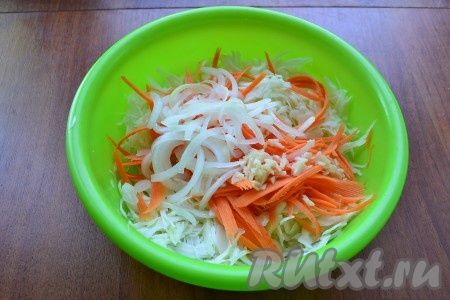 Очищенный лук, нарезанный тонкими полукольцами, и измельченный очищенный чеснок выложить к капусте с морковью и немного подавить руками.