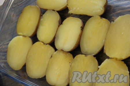 Когда картошка сварится, слить воду. Картофель немного остудить. Каждую картофелину разрезать на две части и выложить половинки в жаропрочную форму (при желании, форму можно смазать маслом).
