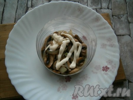 На тарелку выложить остывшие жареные грибы с луком первым слоем, формируя салат с помощью кулинарного кольца, смазать майонезом.