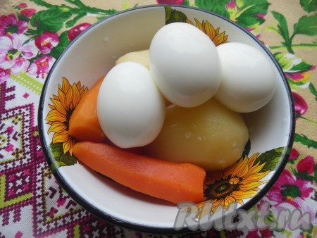 Картофель и морковь тщательно вымойте под проточной водой, затем отварите вместе с кожурой в несоленой воде в течение 30-35 минут. Готовые овощи будут легко прокалываться вилкой или ножом. Воду слейте и залейте на несколько минут вареные овощи холодной водой. Переложите вареный картофель и морковь на тарелку и дайте полностью остыть. Куриные яйца промойте, положите в холодную воду, варите с момента закипания 8-10 минут, чтобы они сварились вкрутую. Переложите яйца в холодную воду, дайте остыть. Очистите остывшие овощи и яйца. Можно сварить все заранее с вечера, а утром быстро очистить и нарезать.

