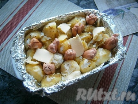 Через 30 минут картофель достать из духовки, вставить половинки сосисок (надрезами кверху) между клубнями картофеля и разложить кусочки сливочного масла.