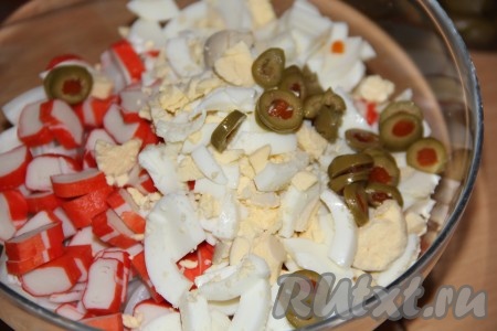 Оливки нарезать тонкими колечками. Соединить нарезанные тушки кальмаров, крабовые палочки, яйца и оливки, перемешать салат и посолить по вкусу.
