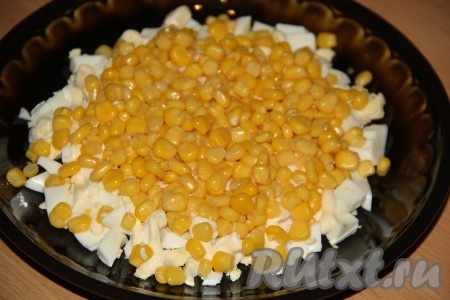 Открыв банку с консервированной кукурузой, слить жидкость. Выложить кукурузу вторым слоем, не забывая, что салат выкладываем горкой и диаметр этого слоя должен быть чуть меньше слоя из яиц.
