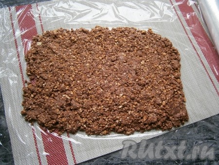 На лист пищевой плёнки выложить массу из печенья в виде прямоугольника, тщательно разровнять.
