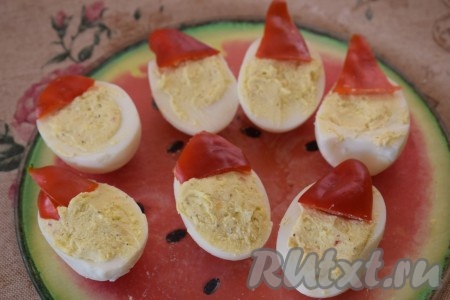 Кладём "шапочки" на верх фаршированных половинок яиц, вдавливая нарезанные треугольники болгарского перца в начинку.

