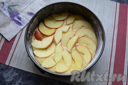 В форму выложить тесто и разровнять его. Сверху в один слой разместить дольки яблок, очищенных от семян.
