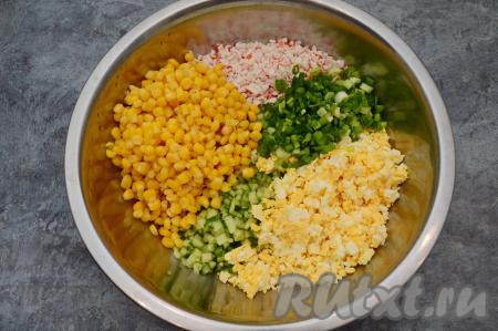 В глубокую миску выложить нарезанные крабовые палочки, зелёный лук, яйца, свежие огурцы, добавить кукурузу, перемешать салат.