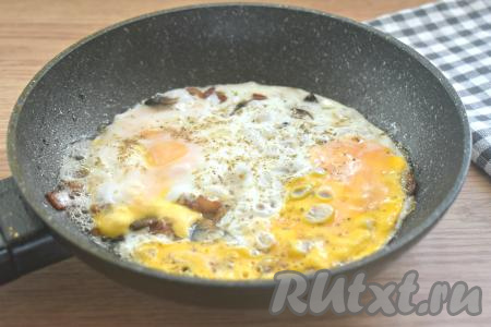Сковороду накрываем крышкой и готовим яичницу с беконом и грибами на огне ниже среднего 3-4 минуты (яйца должны полностью схватиться).