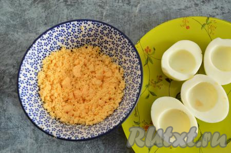 Из половинок яиц вынуть желтки и сложить их в тарелку. Вилкой растереть желтки в крошку.