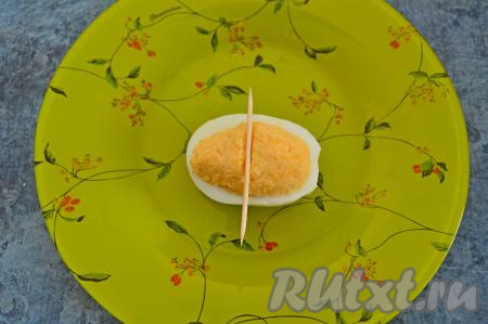 Наполнить половинки яиц сырно-желтковой массой. Начинку из желтков и сыра нужно выкладывать в половинки яиц с небольшой горкой. Затем по середине фаршированной половинки белка зубочисткой сделать небольшое углубление, как на фото.