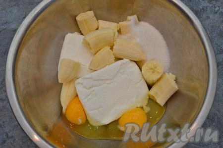 В глубокую миску выложить творог и очищенные от шкурки бананы, разломанные на кусочки, всыпать сахар и вбить сырые яйца.