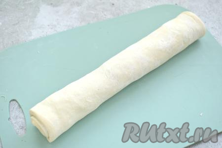 Плотно сворачиваем слоёное тесто с сыром и ветчиной в рулет, начиная со стороны с ветчиной.