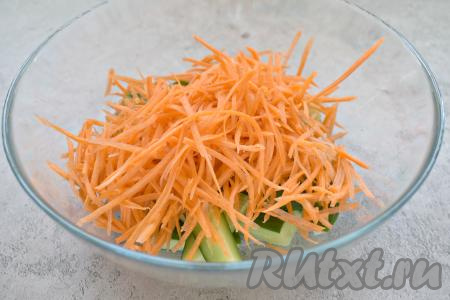 Натираем очищенную морковку на тёрке для моркови по-корейски (если нет такой тёрки, натрите на обычной крупной тёрке или нарежьте на тонкие полоски), перекладываем к огурцам.