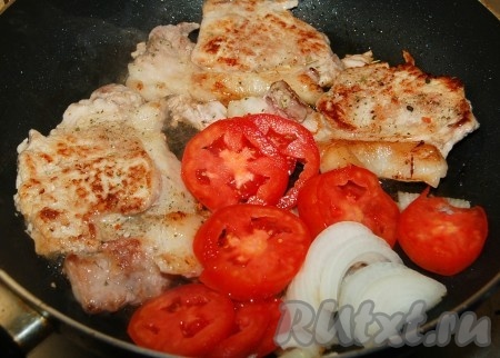 Отбивные из свинины сдвинуть на край сковородки, а рядом с ними разместить помидоры с луком.