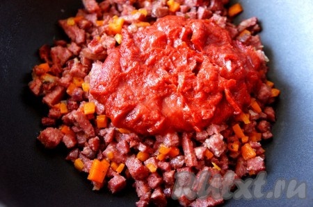 К обжаренным овощам и колбасе добавить томатную пасту, 100-200 мл воды, соль, чёрный молотый перец по вкусу. Перемешать, накрыть крышкой, довести до кипения, а затем тушить на медленном огне около 5 минут.
