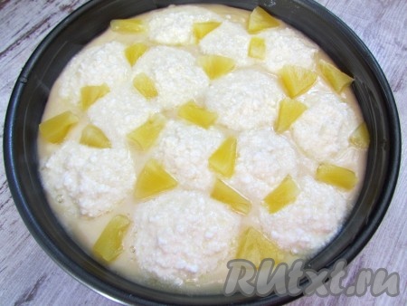Форму смажьте сливочным маслом и выложите тесто. Сверху распределите творожные шарики и кусочки ананаса, слегка вдавив их в тесто.