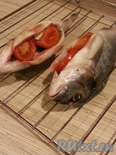 Кладём дорадо на противень спинкой вниз, внутрь брюшка каждой рыбки выкладываем лук, чеснок, укроп и помидоры.