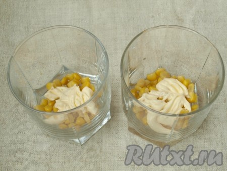 На дно порционных стаканов выложить по 2 столовые ложки консервированной кукурузы. Смазать майонезом.
