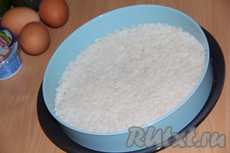 Рис отварить до готовности в подсоленной воде, остудить. Яйца сварить вкрутую, остудить и почистить. На дно плоской тарелки поставить бортики для формирования закусочного торта. Выложить рис, разровнять и смазать майонезом.
