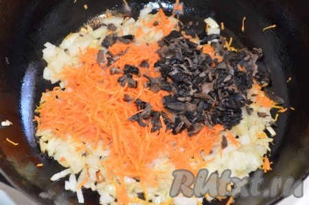 К обжаренному луку выложить очищенную и натёртую на мелкой тёрке морковку, добавить оставшиеся мелко нарезанные грибы, обжаривать 2-3 минуты, помешивая.