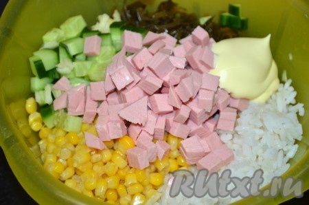 В миску с рисом, кукурузой и морской капустой добавить колбасу, огурец и чеснок, посолить, по желанию, поперчить, заправить салат майонезом (или сметаной).