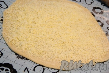 Сыр натереть на мелкой тёрке. Круг, смазанный маслом, посыпать половиной натёртого сыра.