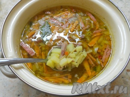 Далее в суп с колбасой добавить вермишель, специи и лавровый лист, если нужно, долить небольшое количество горячей воды и немного посолить. Также добавить измельченный чеснок.
