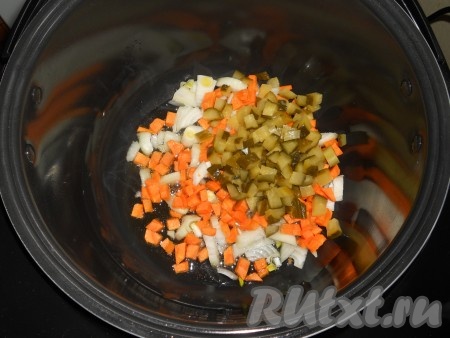 В чашу мультиварки влить растительное масло, выставить программу "Жарка" на 15 минут. Выложить в чашу лук и морковь, добавить нарезанные небольшими кубиками соленые огурцы.

