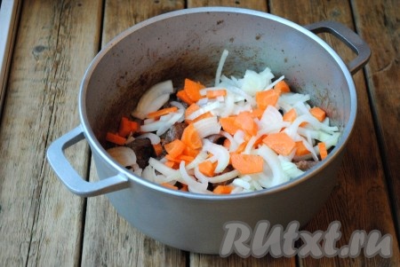 Затем к говядине отправить лук и морковь, нарезанные полукольцами. Жарить, помешивая, 3-5 минут. 
