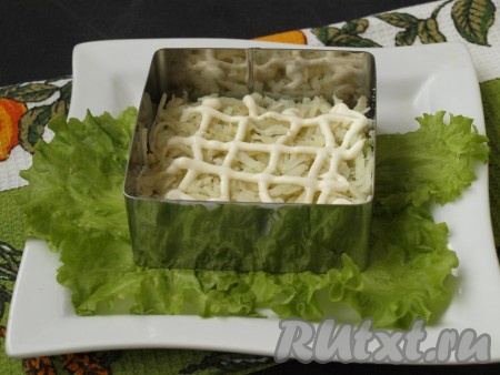 На плоскую тарелку постелить салатные листья, поставить формочку по центру тарелки. Натереть на тёрке очищенную картошку. Выложить половину картофеля на дно, смазать майонезом и немного посолить.