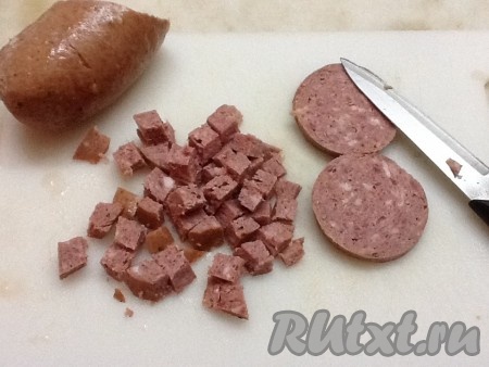 Копченую колбасу нарезать и добавить на сковородку к луку.