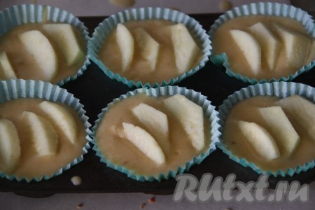 В формы для кексов (силиконовые формочки можно не смазывать маслом) налить тесто, заполняя формы на 2/3. Дольки яблок выложить на тесто, слегка окуная их в него.