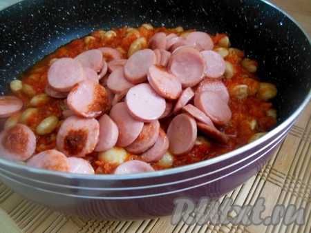 По истечении времени к фасоли в томатном соусе добавьте обжаренные сосиски и тушите еще 3 минуты. По желанию, в конце приготовления, можно добавить несколько измельченных зубчиков чеснока и мелко нарезанную зелень укропа. Уберите сковороду с огня, накройте крышкой и дайте блюду настояться около 30 минут. За это время фасоль пропитается томатным соусом и станет еще более вкусной.