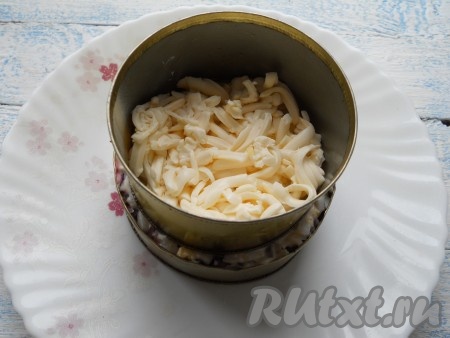 Сверху поместить кулинарное кольцо меньшего диаметра и выложить половину натертого плавленого сыра.
