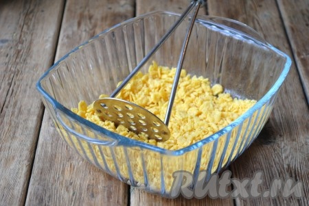 Измельчить кукурузные хлопья, это можно сделать с помощью скалки или толкушки для картофельного пюре. Очень мелко измельчать не нужно. 
