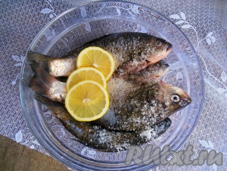 Очищенную рыбу положите в глубокую миску. Для того чтобы в запеченных карасях было меньше мелких косточек, можно на поверхности рыбы (с двух сторон) острым ножом сделать насечки "крест-накрест" от спины к брюшку (в этот раз я решила насечки не делать).  Добавьте соль, черный молотый перец и пару колечек лимона, перемешайте, стараясь выжимать сок из лимона. Оставьте рыбу мариноваться на 10-15 минут.