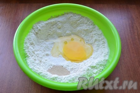 Для приготовления теста в просеянную муку добавить сырое яйцо, соль, сахар и сухие дрожжи.