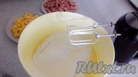 Добавить разрыхлитель, муку, перемешать, получившееся тесто по консистенции будет напоминать густую сметану. Затем добавить в тесто сыр и колбасу, перемешать.