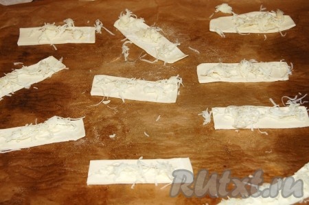 Переложить палочки из слоеного теста на противень, застеленный бумагой для выпечки, и сверху посыпать натертым сыром.
