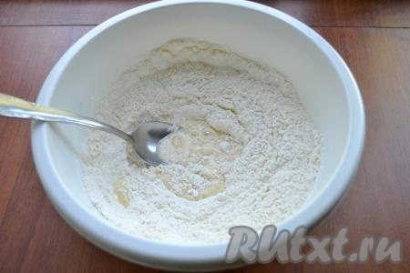 В миску с молочной смесью всыпать соду и начать постепенно добавлять муку, каждый раз полностью вмешивая её в тесто. Сначала перемешивать тесто столовой ложкой, а когда тесто начнёт собираться в ком, начать вымешивать его руками.