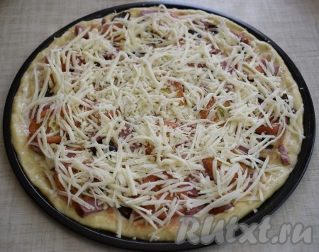 Обильно посыпаем пиццу сыром, натертым на крупной терке.
