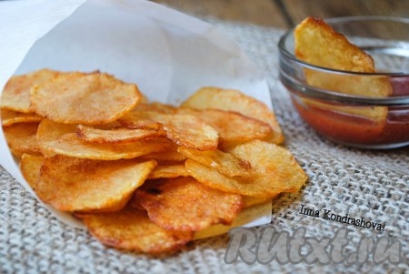 Картофельные чипсы, приготовленные в духовке, остудить, выложить в миску и можно подавать на стол. Аппетитные, хрустящие чипсы очень вкусно подавать с кетчупом.
