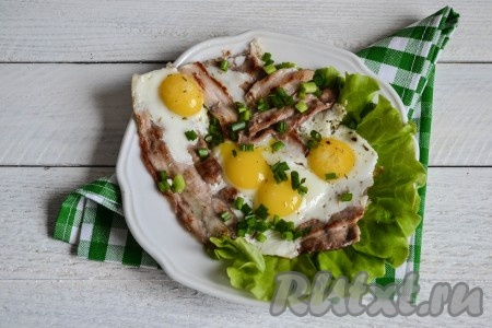 Вкусный и сытный завтрак готов. Выложить на блюдо яичницу с беконом, присыпать нарезанным зеленым луком и сразу же подать на стол.