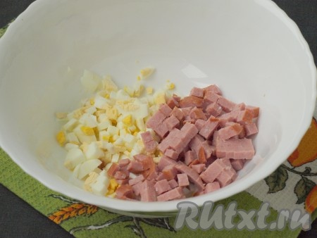 Нарезать кубиками полукопчёную колбасу и очищенные варёные яйца. Сложить их в глубокую миску.
