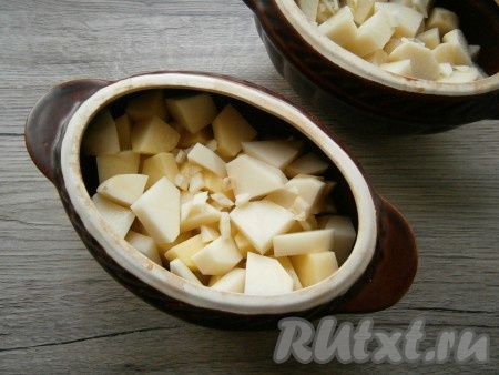 В горшочки с говядиной выложить картофель, нарезанный кубиками, сверху посыпать измельченным чесноком.
