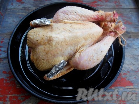 На противень, смазанный растительным маслом, выложите тушку курицы спинкой вниз. Перевяжите ножки курицы шпагатом, оберните кончики крыльев и ножек фольгой.
