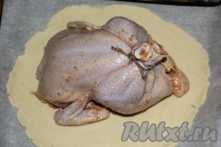 Затем выложить курицу на тесто. Ножки можно завязать ниткой или бечевкой, брюшко можно скрепить зубочистками.