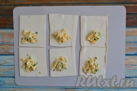 Ближе к одному из уголков каждого квадрата выложить 1 столовую ложку начинки из сыра и яиц.
