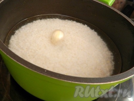 В кастрюлю высыпать промытый рис, залить 2 стаканами холодной воды, выложить вымытый неочищенный зубчик чеснока и поставить на огонь.
