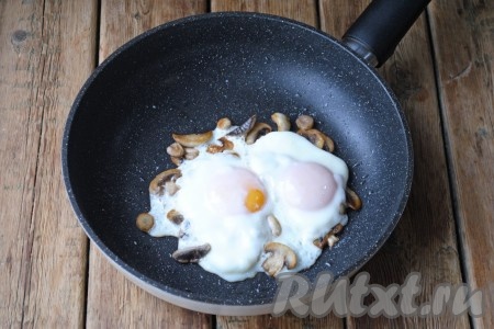 Яйца посолить, накрыть сковороду крышкой и жарить яичницу с шампиньонами на медленном огне 5 минут. За это время белок "схватится", а желток внутри останется жидким. Если вы любите более плотный желток, жарьте на 2 минуты дольше. 